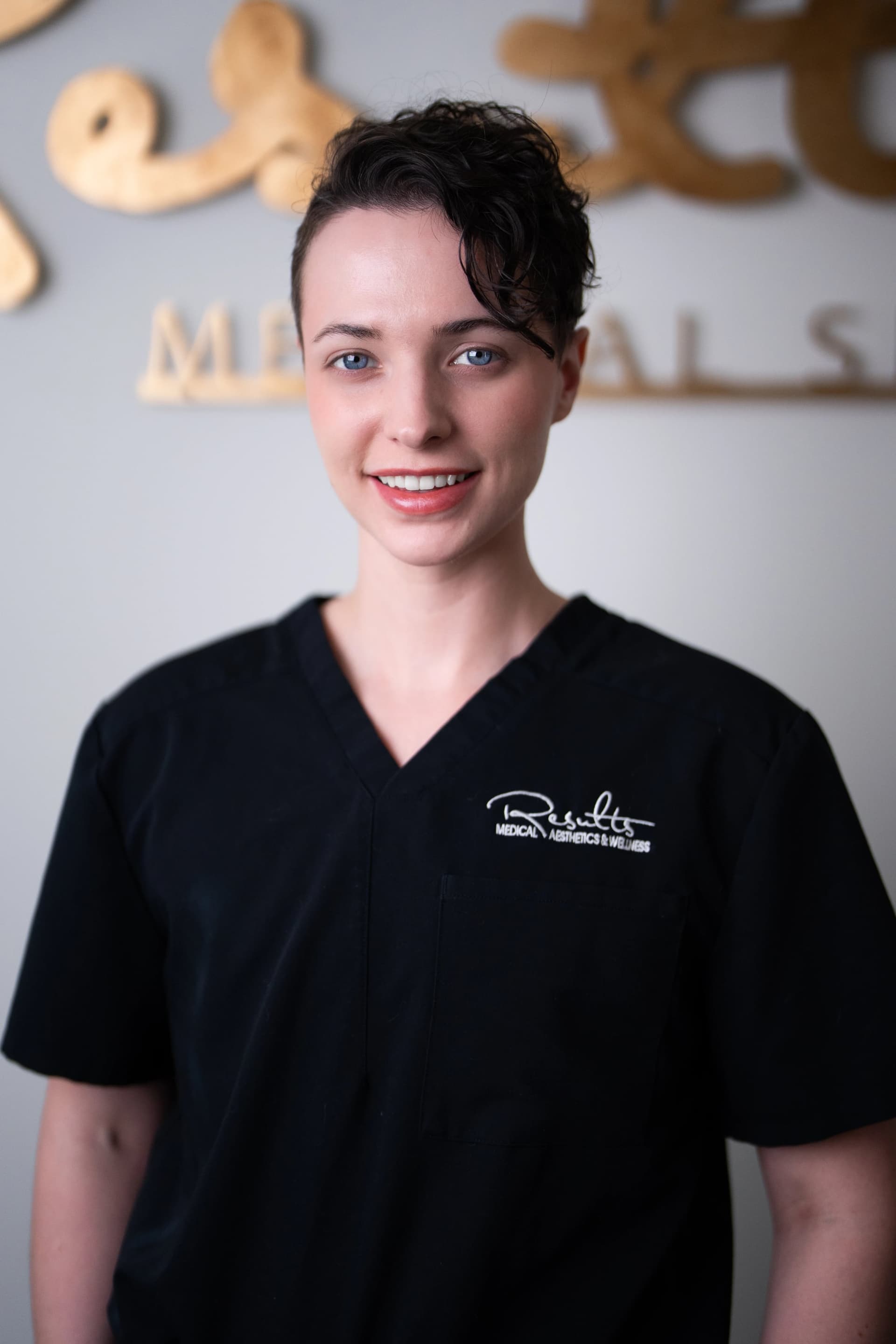 Female staff member portrait in front of the gold Results wall sign