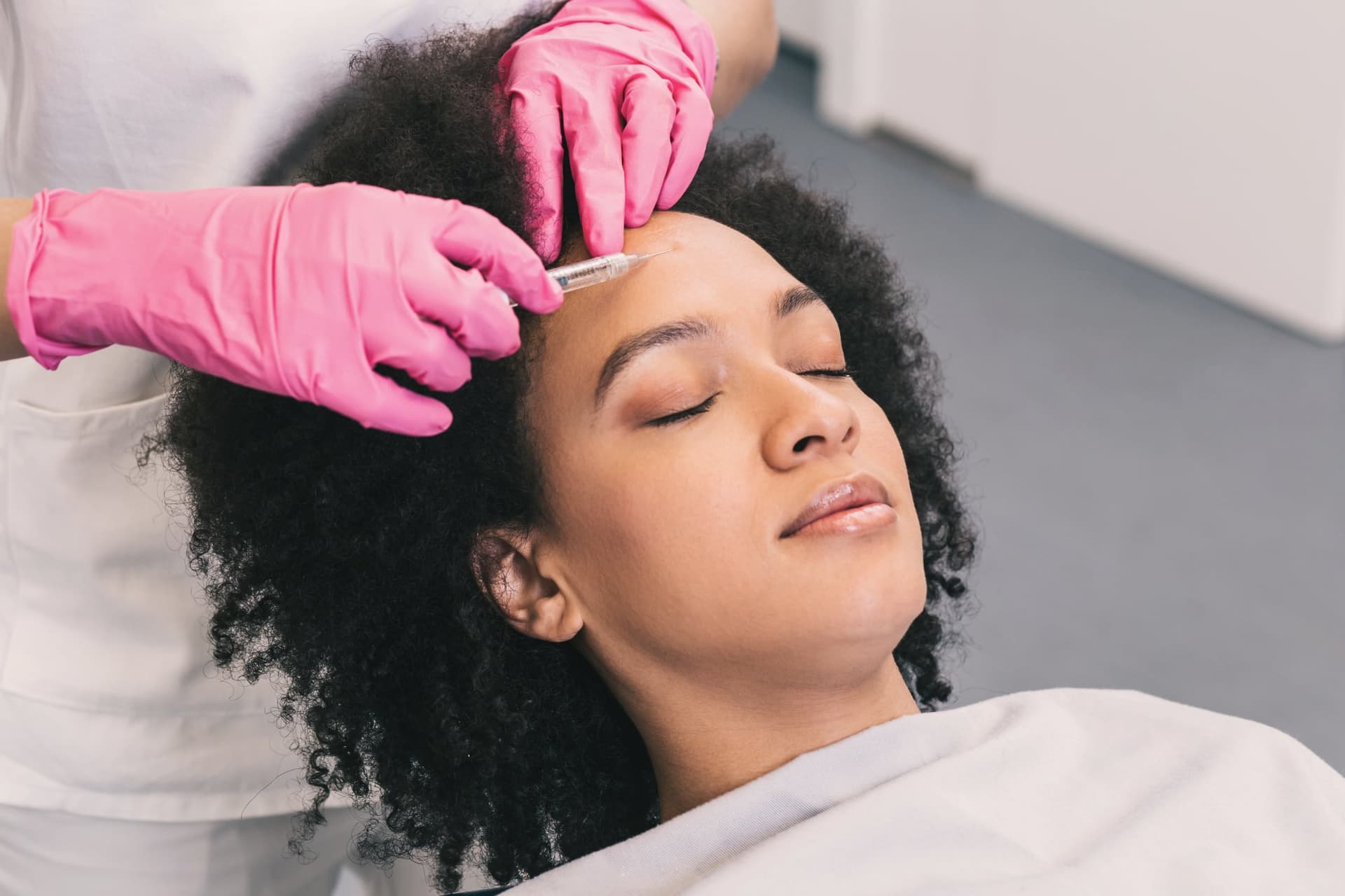 Provider in pink gloves injecting a smiling woman's forehead