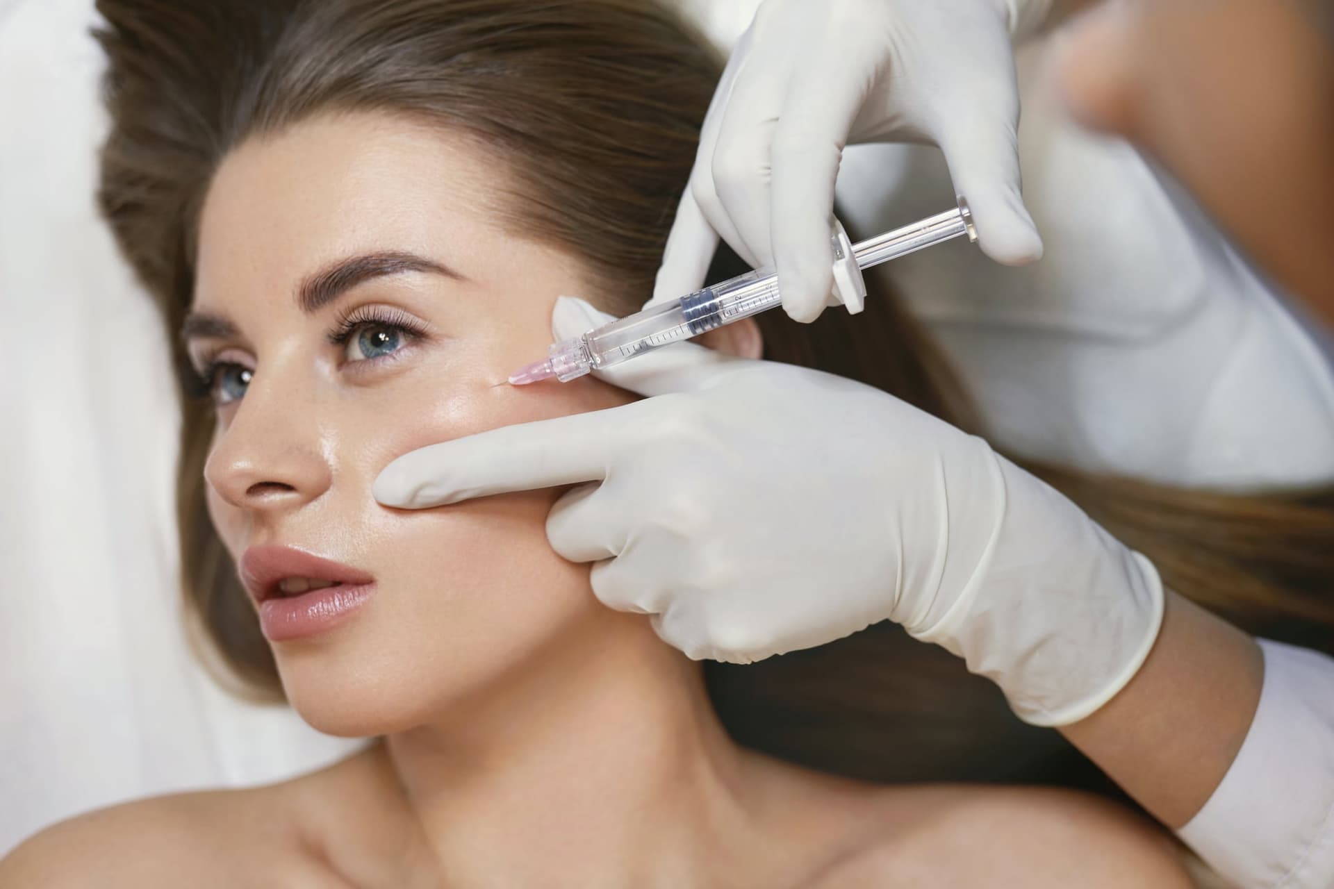 Gloved provider injecting filler near a woman's brow and eye area