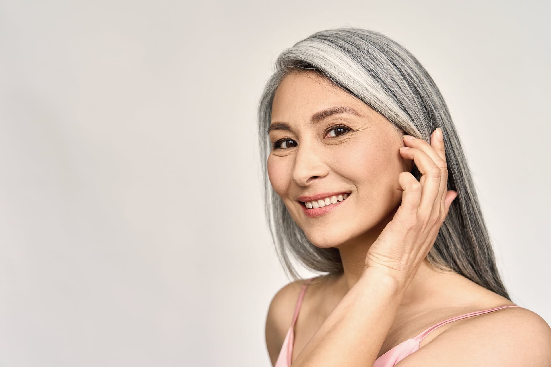 Smiling mature woman with gray hair touching her face, studio portrait