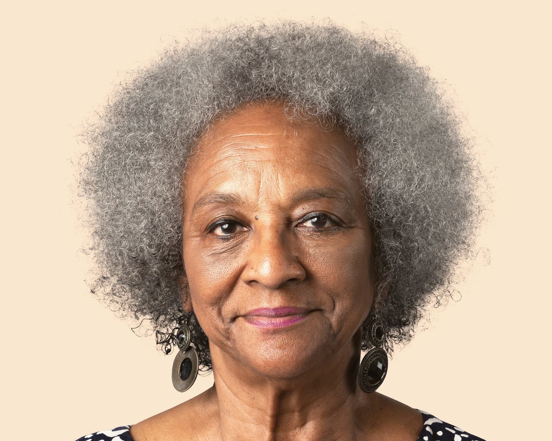 Smiling senior woman with a gray afro against a peach backdrop