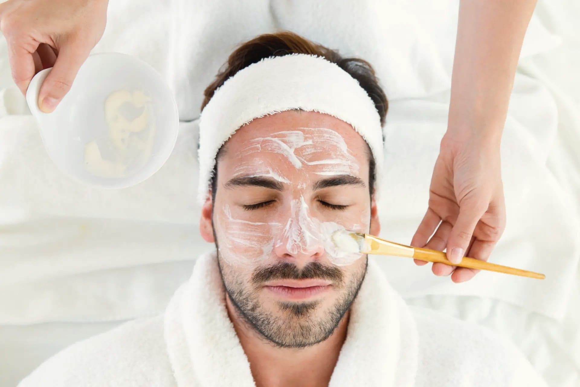 Esthetician applying a facial mask to a man's face, overhead view