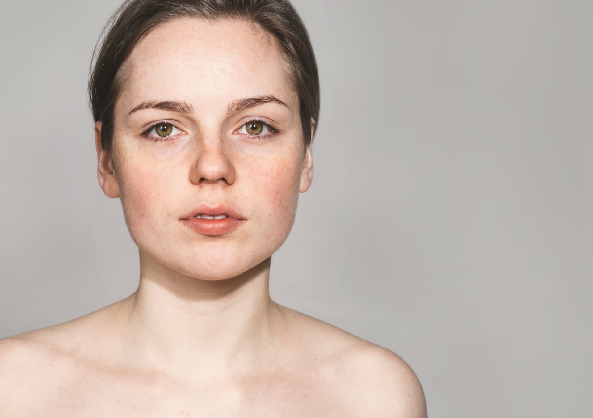 Freckled young woman with bare shoulders in a natural studio portrait