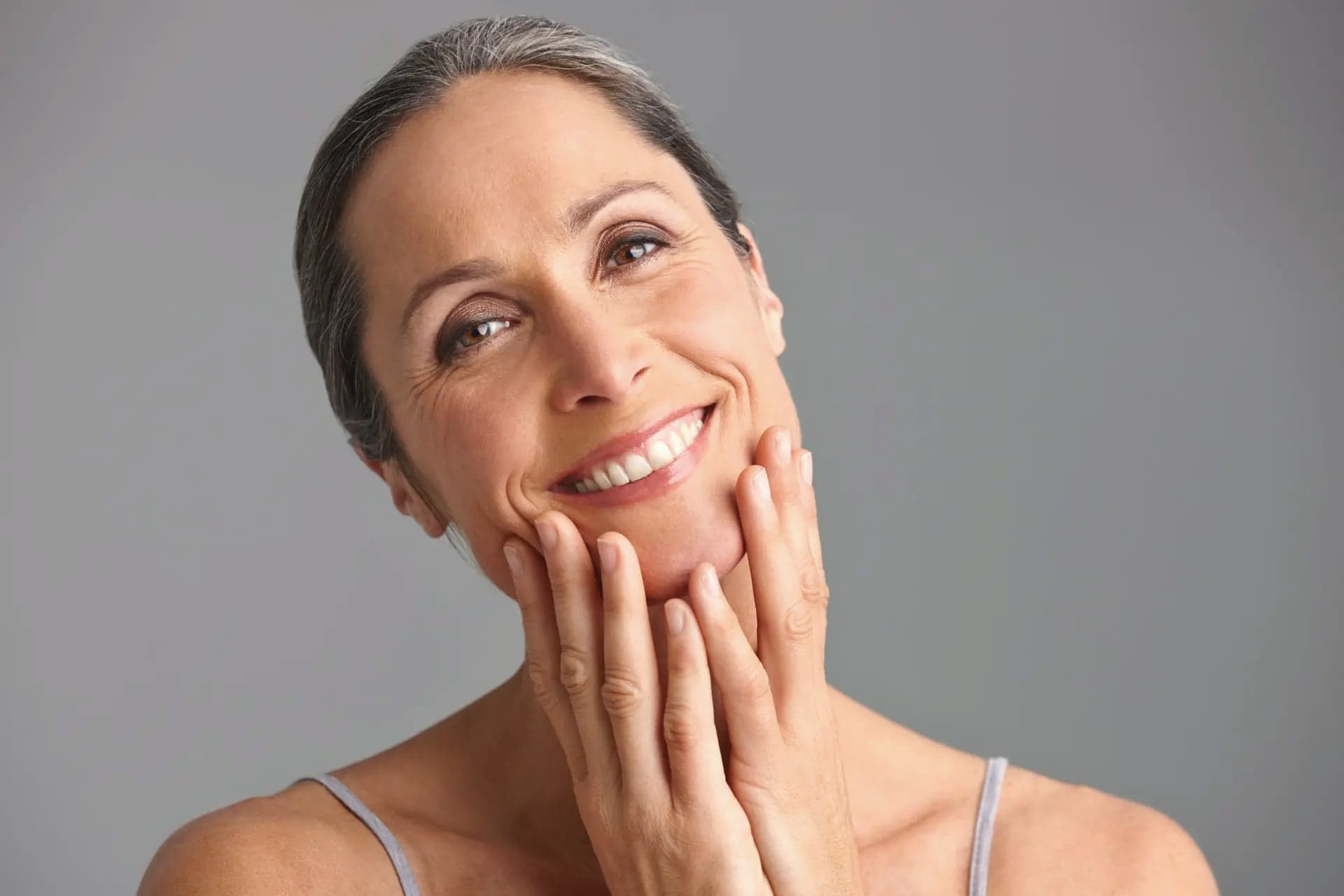 Mature woman with both hands framing her jawline, smiling