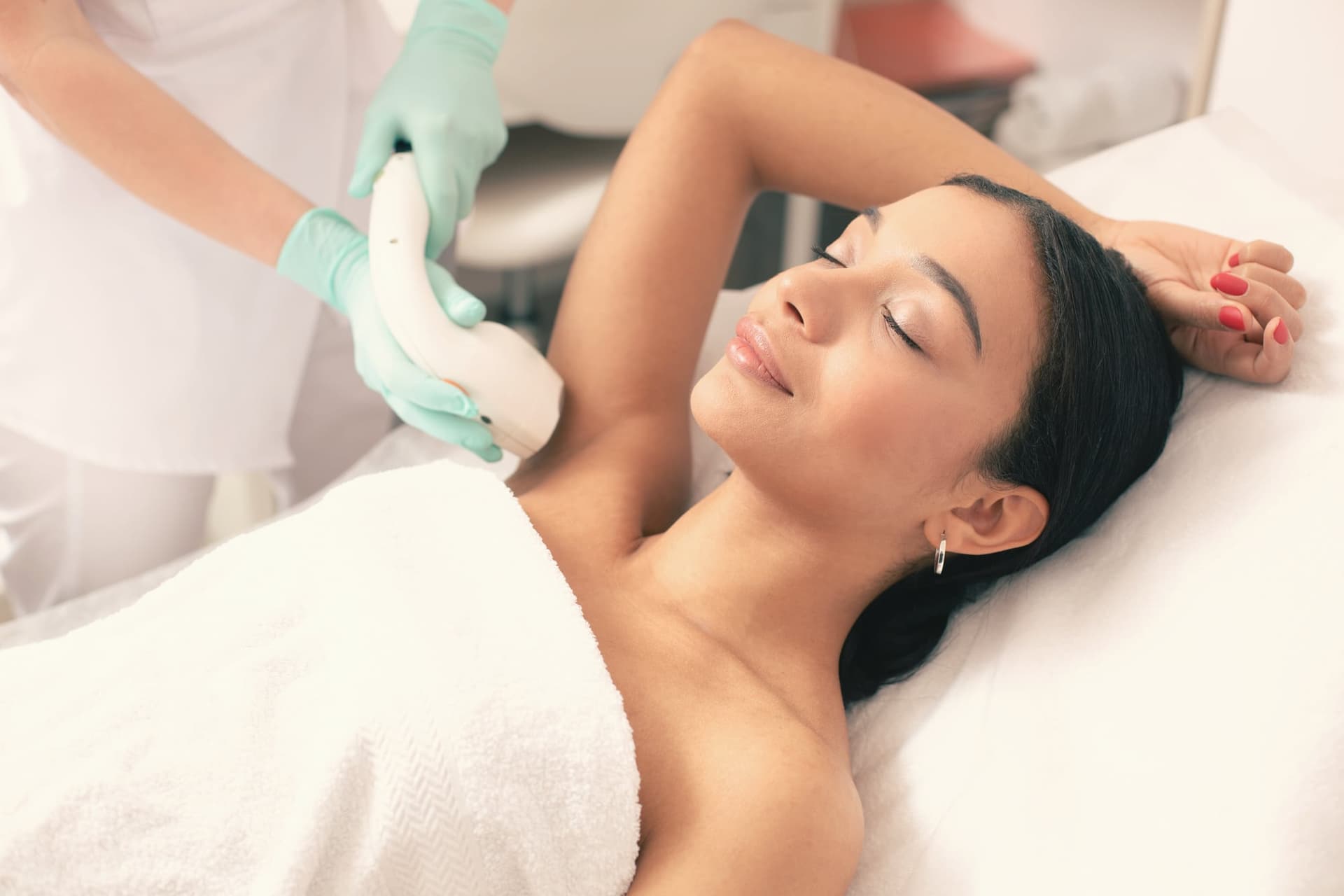 Esthetician performing laser hair removal on a woman's underarm