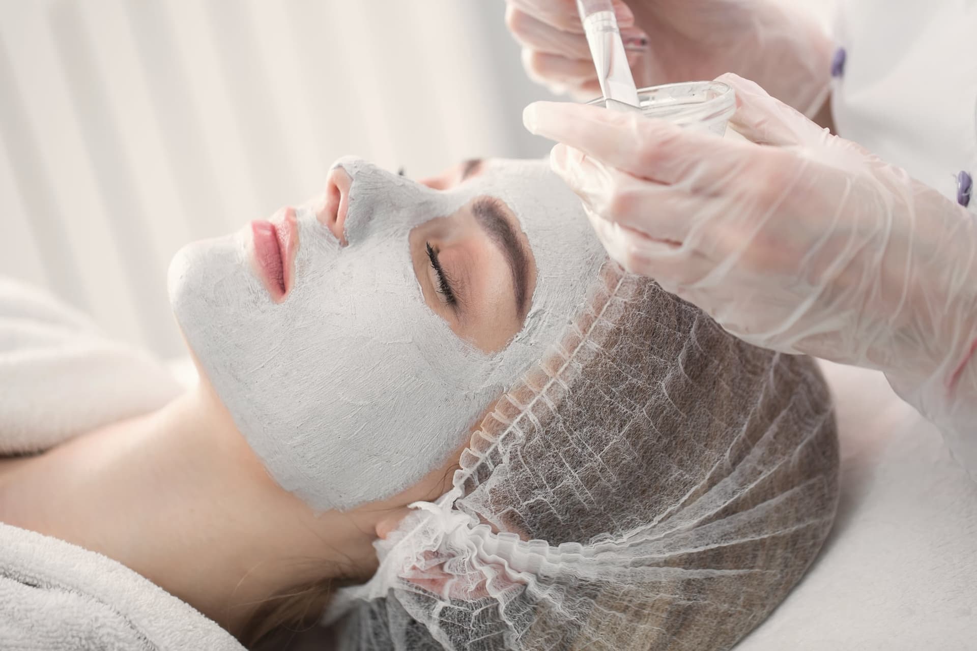Esthetician applying a white clay peel mask to a client's face
