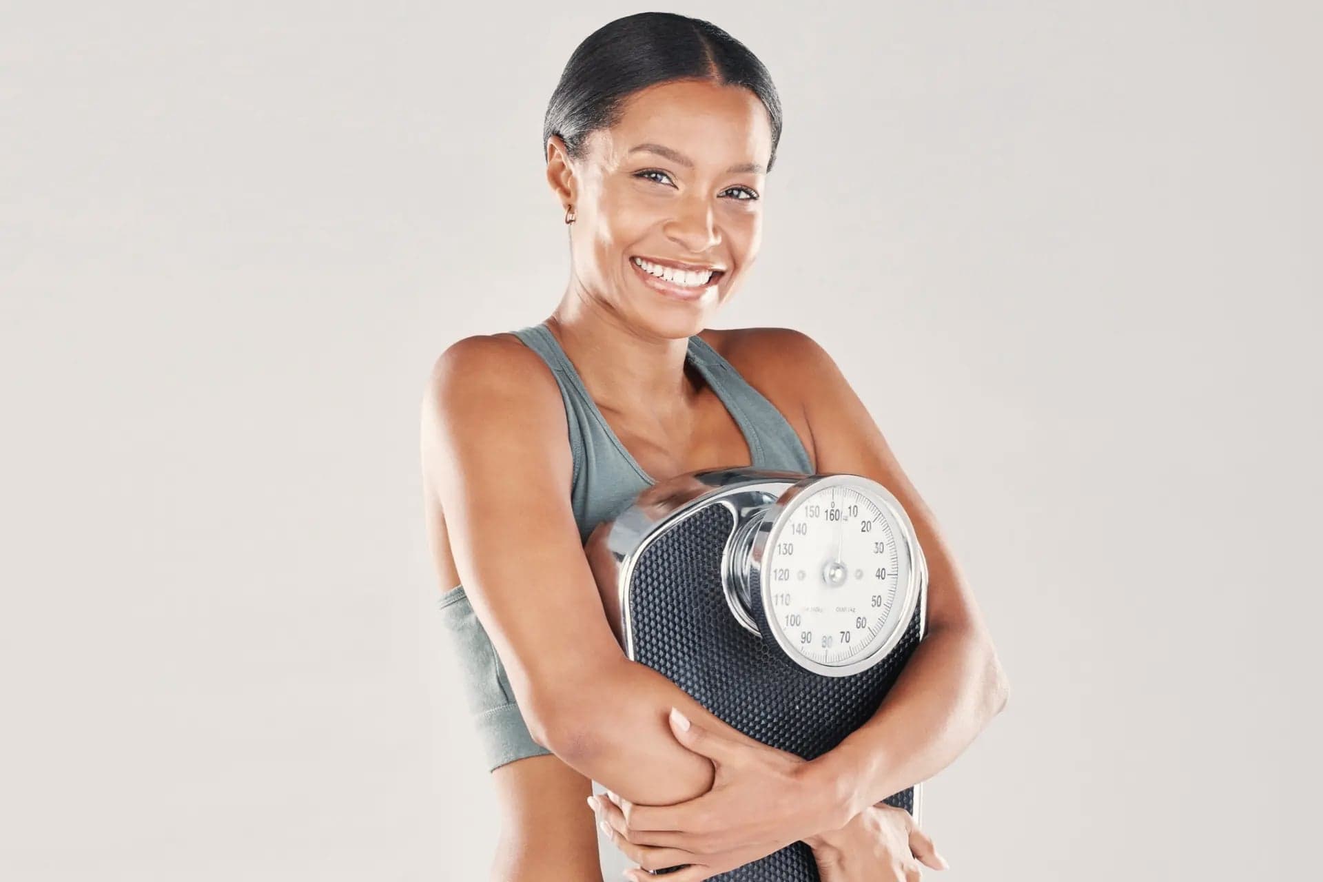 Smiling woman in a sports bra hugging a bathroom scale