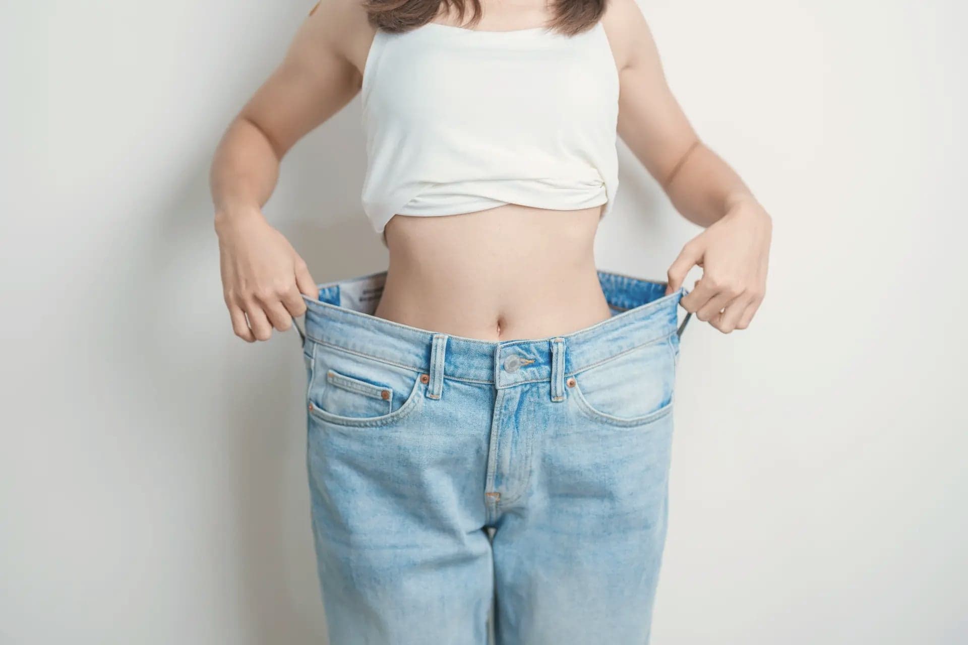 Woman holding out an oversized pair of jeans at her waist