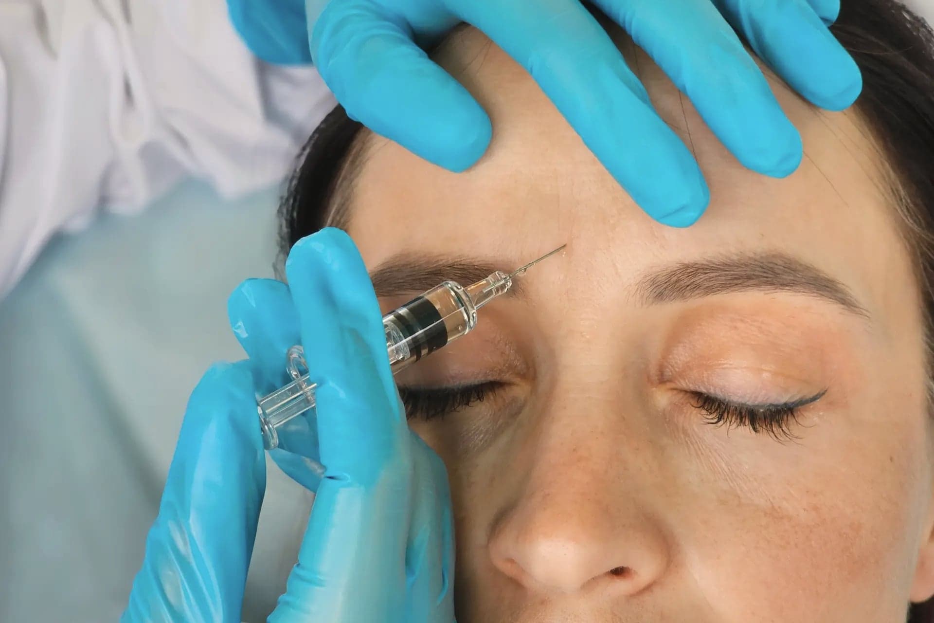 Provider in teal gloves injecting a woman's forehead