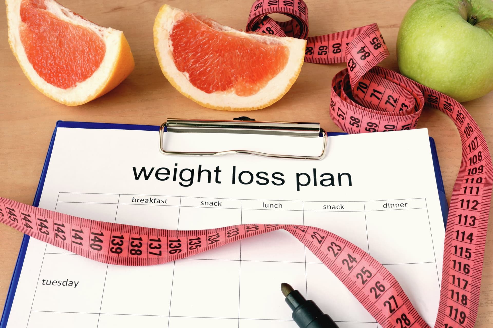 Weight-loss meal-plan clipboard with grapefruit, apple, and tape measure