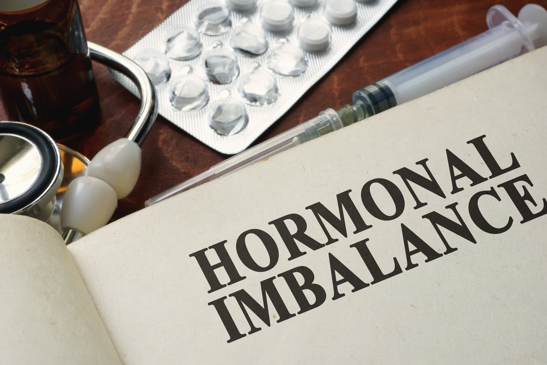 Book titled Hormonal Imbalance beside a stethoscope and pill blister pack